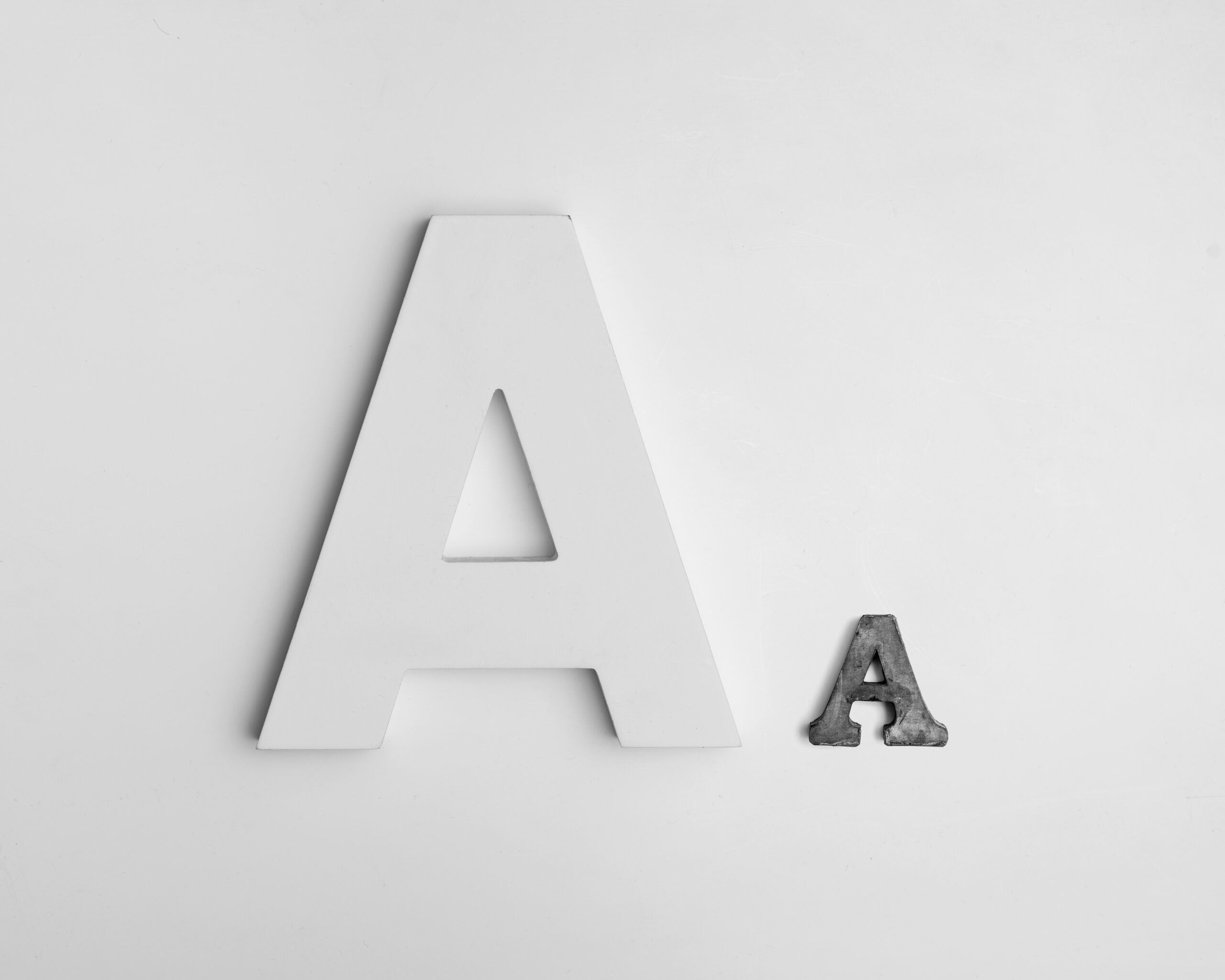 Ein großes weißes und ein kleines graues "A" nebeneinander, dekoratives Bild von zwei Buchstaben
