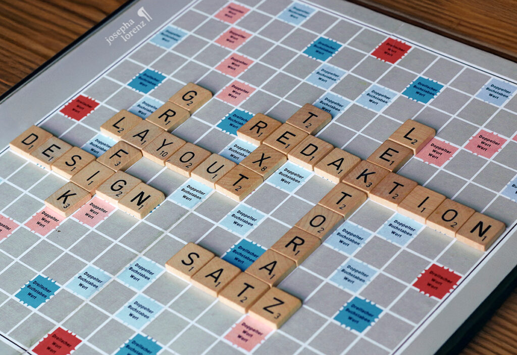 Viele Scrabble-Buchstaben, die die Wörter "Text", "Lektorat", "Redaktion", "Design", "Grafik", "Satz" und "Layout" ergeben und die Leistungen von Josepha Lorenz zeigen